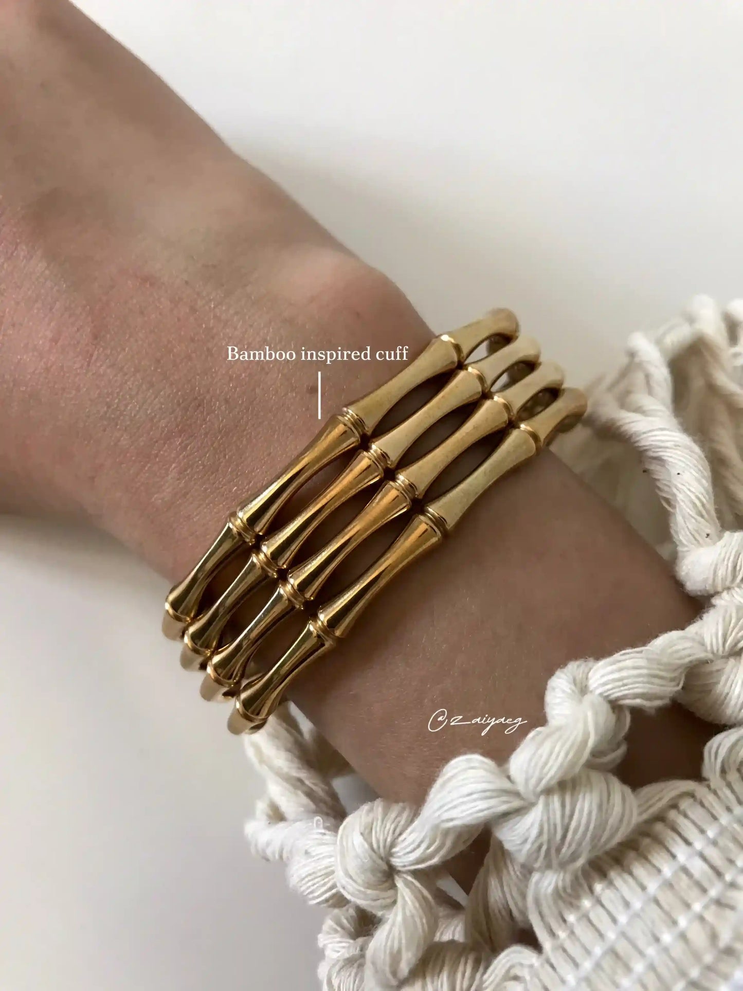 Gold bamboo inspired cuff bracelet on wrist with cream macrame sleeve