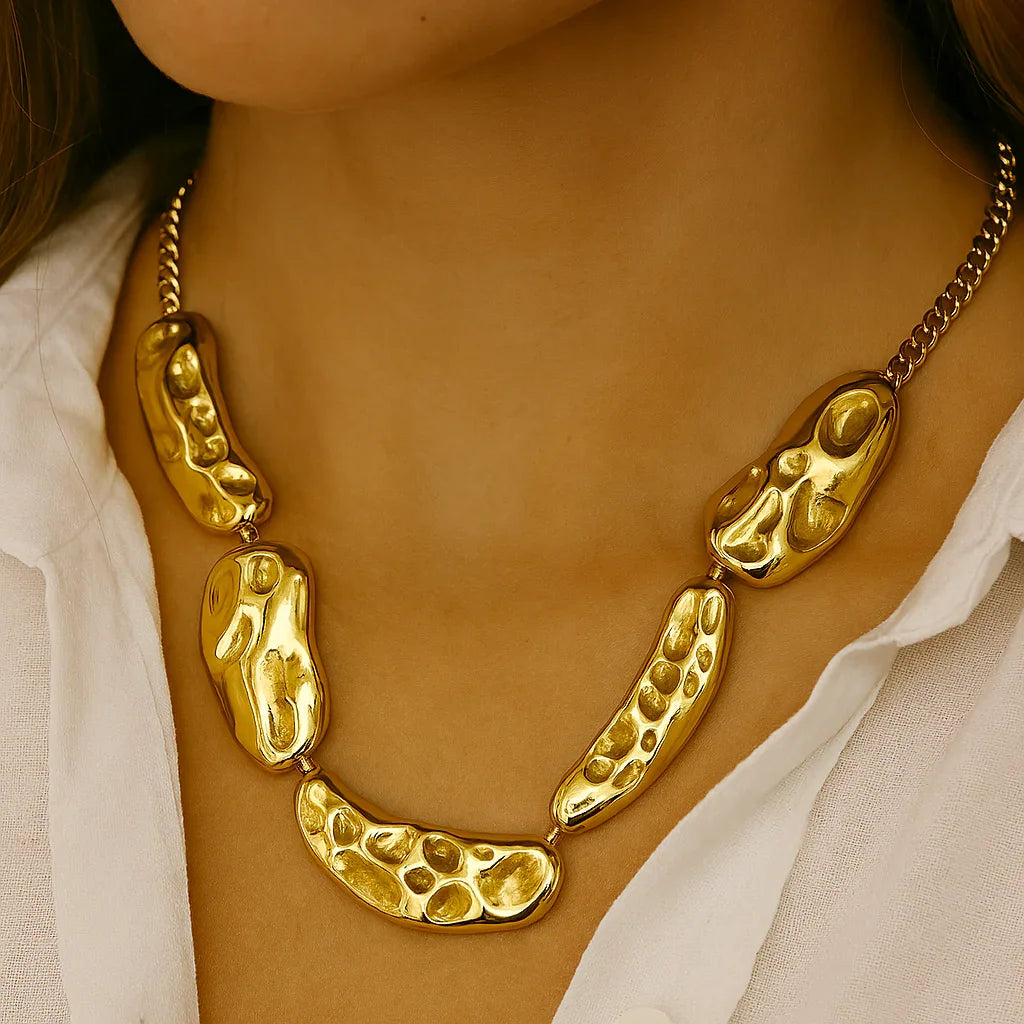 Chunky textured gold necklace on woman wearing white shirt, statement jewelry