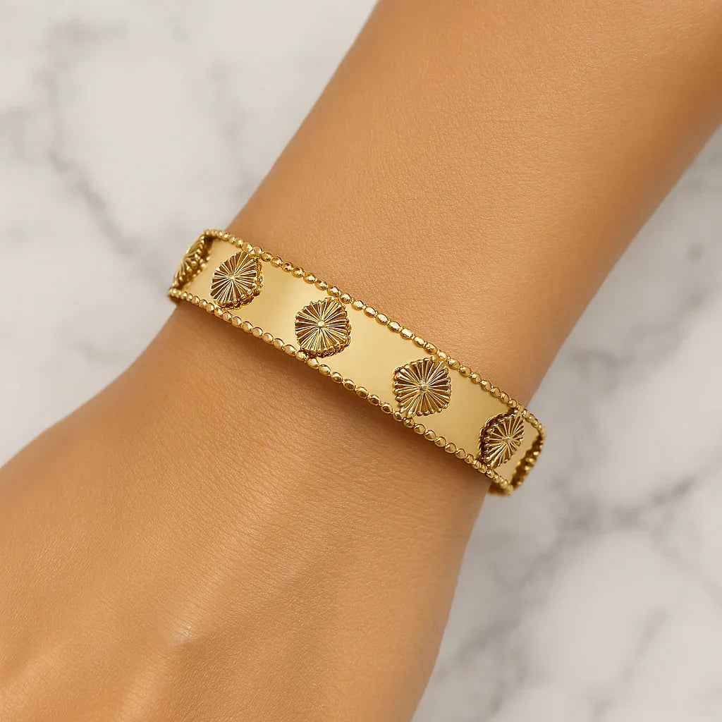 Gold Van Cleef style bracelet with floral motifs on wrist, marble background